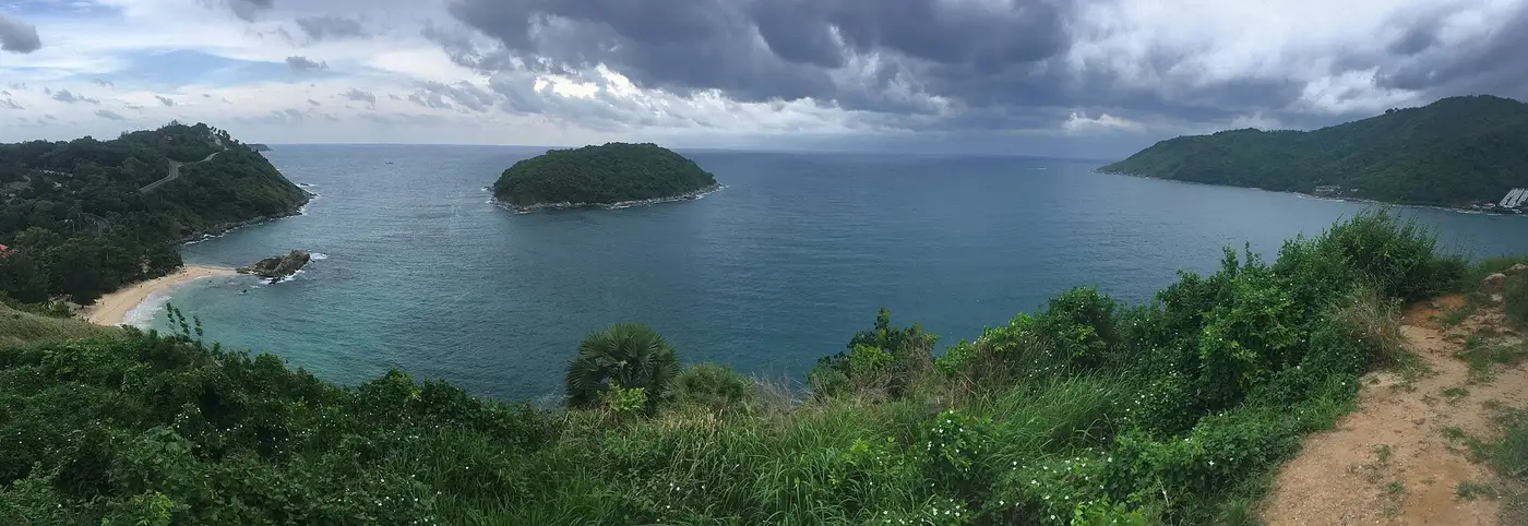 Panorama over Phuket's southern coast from the Windmill Viewpoint, with a forested island offshore and sand along the bays