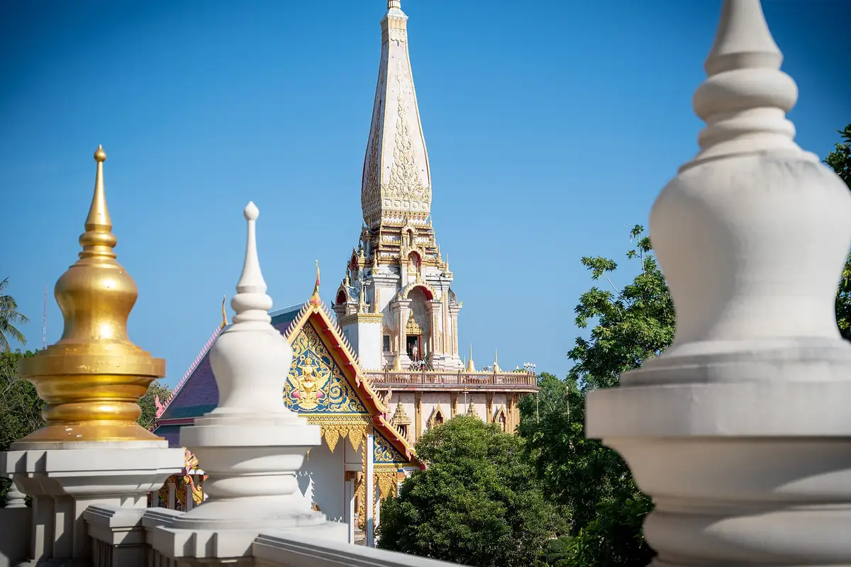 The white and gold chedi spire of Wat Chalong temple rising above smaller stupas under a clear blue sky